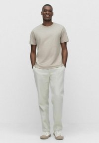 Lys beige crewneck t-shirt med korte ærmer, parret med lys grønne bukser og beige sneakers, alt i en enkel, afslappet stil.