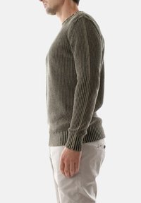 Maglione grigio a coste con maniche lunghe, caratterizzato da un collo rotondo e un tessuto testurizzato, indossato su pantaloni chiari.