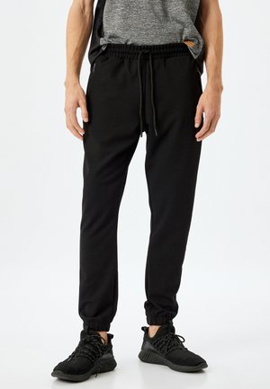 Zwarte joggingsbroek van zacht materiaal, met een elastische tailleband met trekkoord, zijzakken en taps toelopende boorden.
