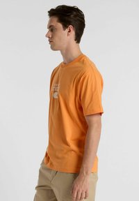 Orange cotton t-shirt with short sleeves. Features a white printed logo "NEW ATH." across the chest. Simple, relaxed fit design.