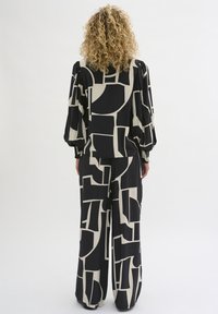 Bluză și pantaloni largi, cu un model în culorile negru și crem. Prezintă forme geometrice și un material moale, cu mâneci bufante și manșete elastice.