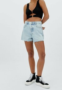 Top corto negro de canalé con detalle retorcido, combinado con pantalones cortos de mezclilla de tiro alto en azul claro con dobladillo deshilachado y bolsillos frontales. Zapatillas negras de caña alta.