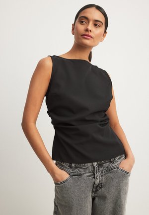 Sort ærmeløs top med en afslappet pasform, lavet af glat stof, med en rund halsudskæring og subtil drapering. Kombineret med grå denim bukser.