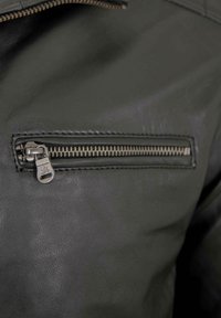 Dunkelgrüne Lederjacke mit einer Reißverschluss-Tasche und silbernem Reißverschluss, strukturierter Oberfläche und subtiler Glanz.