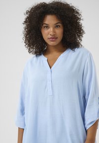 Lichtblauw linnen shirt met een V-hals, driekwart mouwen en een knoopsluiting. Zachte textuur en ontspannen pasvorm.