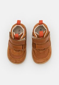 Browningās ādas un zamšādas zīdaiņu kurpes ar divām Velcro siksnām, noapaļota forma, kontrastējošas tekstūras un oranžiem cilpām uz papēža.