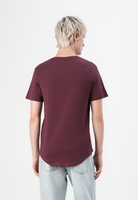 Burgunderfarbendes T-Shirt mit Rundhalsausschnitt und kurzen Ärmeln, aus weichem Baumwollstoff gefertigt, mit abgerundetem Saum und minimalistischem Design.