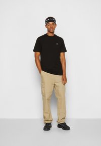 Black cotton t-shirt with a small logo, paired with beige cargo pants featuring multiple pockets and wearing black sneakers.