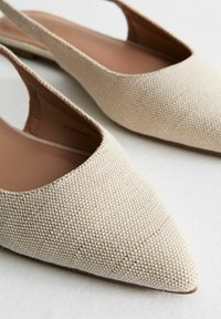 Beiga slingback-skor med spetsig tå, texturerad ovandel i tyg och en slät innersula. Flat såldesign för enkel användning.