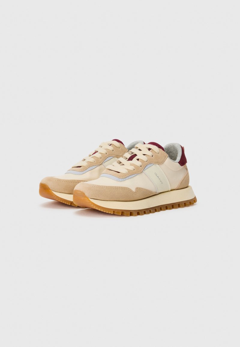 Beige und cremefarbene Sneaker mit Gummisohlen, hellbraunen Wildlederelementen und burgunderroten Details an Ferse und Zunge, nebeneinander gezeigt.