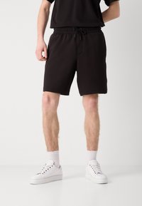 Shorts neri in cotone misto con vita elastica e cordoncino. Taglio dritto, lunghezza fino al ginocchio, abbinati a sneakers bianche e calze corte.