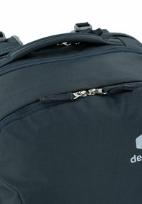 Mochila negra con superficie textil suave, asa en la parte superior y compartimento con cremallera con tirador metálico. Logo de la marca exhibido.