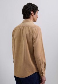 Brązowa bawełniana koszula z kołnierzykiem na guziki, długimi rękawami i zaokrąglonym dołem. Charakteryzuje się luźnym krojem i subtelną teksturą.