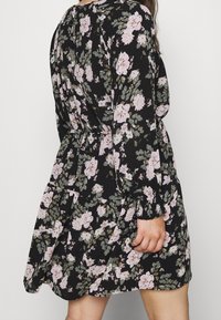 Florales Kleid in Schwarz mit pinken und grünen Blumen, langen Ärmeln, taillenbetontem Schnitt und ausgestelltem Rock. Verfügt über einen strukturierten Stoff und geraffte Ärmel.