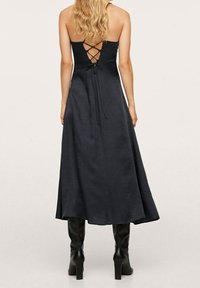 Mustassa hihattomassa mekossa on keskivälin hame, jossa on nauhasta säädettävä selkäosa ja sileä pinta. Yhdistetty polviin asti ulottuviin mustiin saappaisiin.