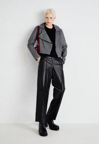 Giacca grigia cropped con colletto a revers, abbinata a pantaloni in pelle nera a vita alta e stivali neri con plateau, accentuata da una borsa rossa.