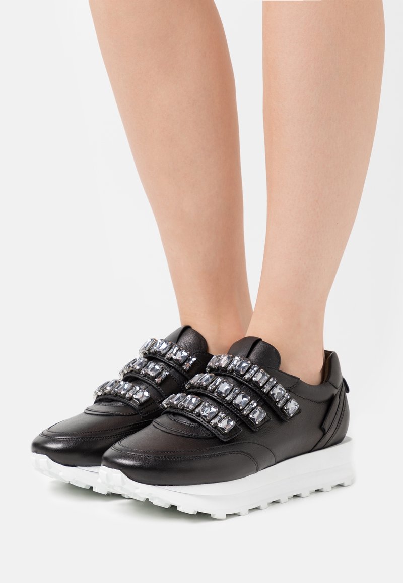 Svarta lädersneakers med tre Velcro-remmar prydda med ädelstenar, vit plattformssula och texturerad yttersula för bra grepp.