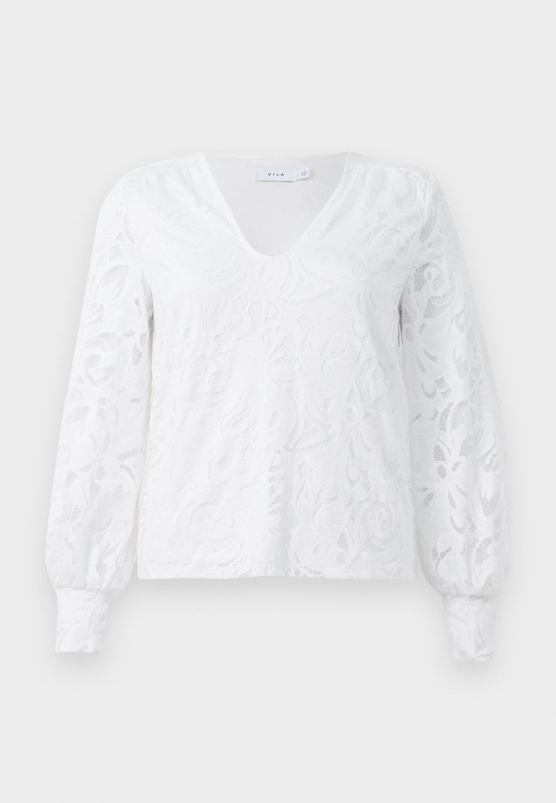 Haut à manches longues blanc avec décolleté en V, présentant un design en dentelle florale texturée et des poignets froncés. Fabriqué en tissu léger.