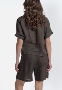 Bruine linnen tweedelige set bestaande uit een shirt met korte mouwen en shorts, met een relaxte pasvorm en opgerolde mouwen. Zachte textuur en minimalistisch ontwerp.