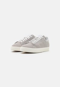 Sneaker grigie chiare in suede, con lacci bianchi, suola in gomma texture e piccoli fori di ventilazione sui lati.