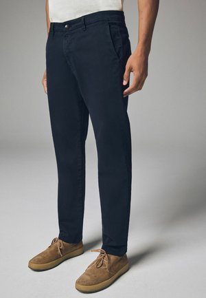 Chinos marino en twill de algodón ligero con corte recto, parte delantera plana y bolsillos laterales, combinados con zapatos de ante marrón.