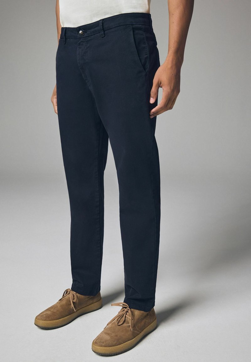 Chinos blu navy in twill di cotone leggero con taglio dritto, frontale piatto e tasche laterali, abbinati a scarpe in suede marroni.