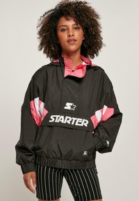 Zwarte windbreaker jas met roze en witte accenten, voorzien van een hoge kraag, elastische manchetten en een logo op de voorkant.