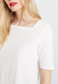 Camiseta de crew neck blanca con mangas cortas, que presenta un escote ligeramente cuadrado y una suave y lisa tela de algodón.