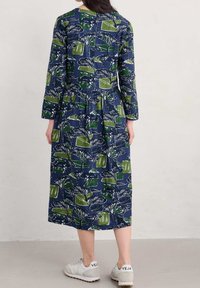 Långärmad, marinblå klänning med grön och vit botanisk tryck, lager-på-lager design, tillverkad av bomull. Matchas med neutrala sneakers.