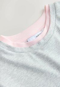 Gros plan sur le col d'un sweat-shirt gris superposé à un col rond rose, montrant la texture du tissu et une partie d'une étiquette de vêtement blanche.