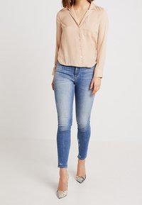Light beige button-up blouse, sheer fabric, collar and pocket detail, paired with blue skinny jeans, and snake-patterned high heels.