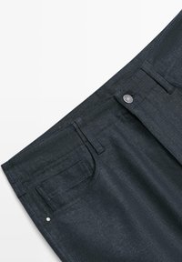 Donkerblauwe spijkerbroek taille met voorzakken, riemlussen en een metalen knoopsluiting tegen een witte achtergrond.