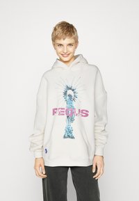 Sudadera con capucha blanca que presenta un gráfico azul de la Estatua de la Libertad con la palabra "PEOUS" en letras mayúsculas de color rosa neón. Incluye un bolsillo canguro.