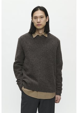 Suéter marrón texturizado con cuello redondo sobre una camisa color beige claro con cuello; combinado con pantalones oscuros y ajustados. Look casual en capas.