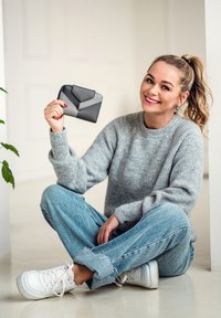 Black and gray wallet with a folded design held in a hand, sitting against a light background, paired with a gray sweater and denim jeans.