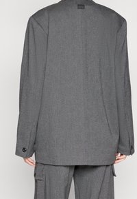 Szary żakiet o dopasowanym kroju z teksturowanej tkaniny, w oversize'owym kształcie, z klapami i guzikami na rękawach.