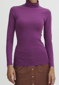 Lila långärmad polotröja tillverkad av mjukt, stretchigt tyg med en figurnära design. Halsringningen är hög och ärmarna är åtsittande.