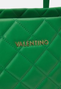 Quiltad grön läderhandväska med en gyllene "Valentino"-logotyp. Slät ytfinish med diamantformad mönstring och matchande sömmar.