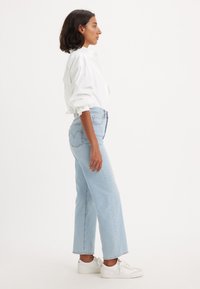 Jeans de cintura alta azul-claro com um design de perna reta, apresentando um fecho de botão e dois bolsos traseiros. Combinados com uma camisa branca de botão e ténis brancos.