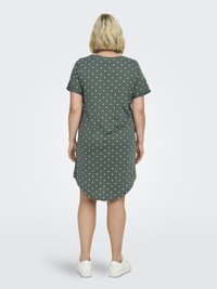 Grön kortärmad klänning med vita prickar, rundad nederkant och avslappnad passform, gjord av mjukt tyg. Bärs med vita sneakers.