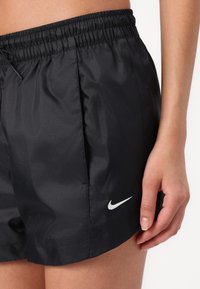 Black Nike shorts made from smooth nylon, featuring an elastic waistband, side pockets, and a white Nike logo on the left leg.