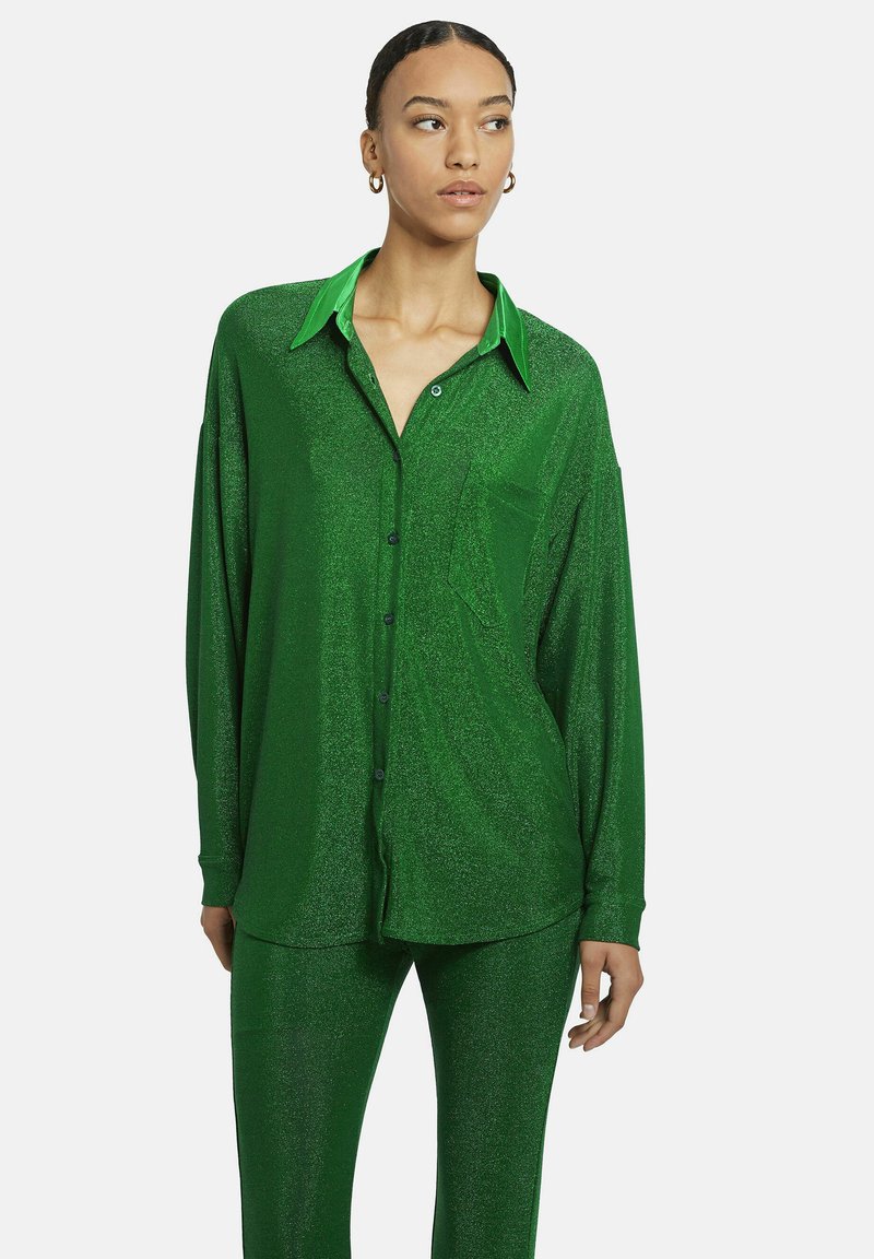 Grüne, schimmernde Button-up-Hemd mit engem, grünem Kragen, lockerer Passform, langen Ärmeln und einer Brusttasche, kombiniert mit passenden Hosen.