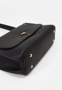 Black textured handbag with a flap closure, gold hardware accents, and four gold studs on the base. Compact rectangular design.