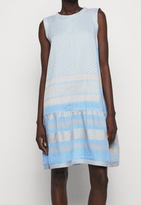 Hellblaues ärmelloses Kleid mit strukturierten Mustern, einem ausgestellten Schnitt und einem Rüschensaum mit horizontalen Streifenakzenten.