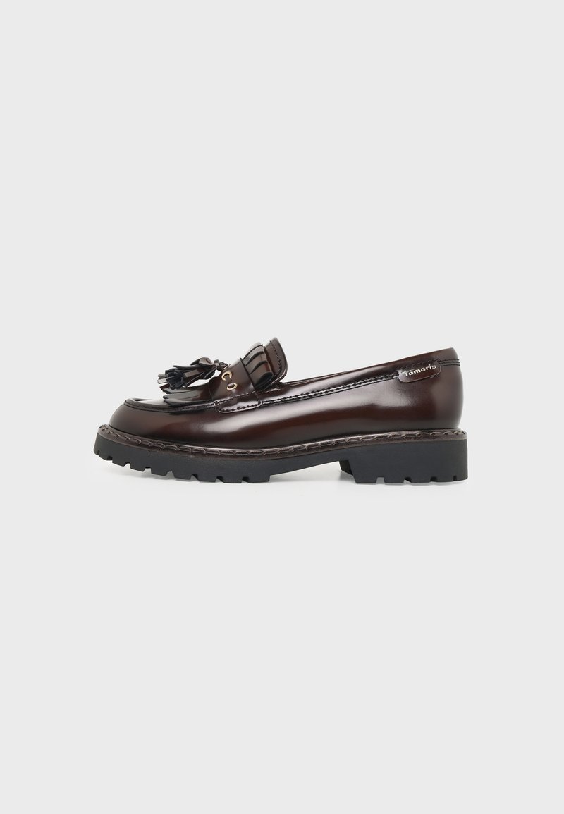 Mocassin en cuir marron foncé avec pampilles, semelle épaisse noire à relief, et couture décorative, présenté sur un fond clair uni.
