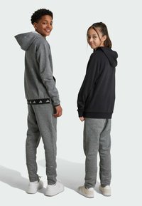 Sudaderas con capucha en gris y negro con pantalones de chándal a juego, que cuentan con puños y cintura elásticos, y acentos de zapatillas blancas.