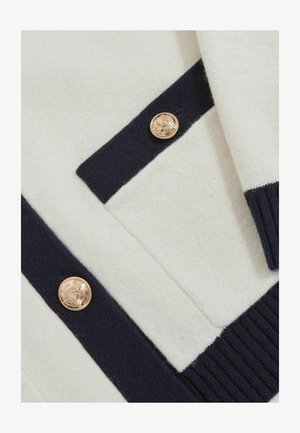 Maglione a maglia in crema e blu navy con tessuto testurizzato, caratterizzato da bottoni dorati e strisce a contrasto lungo i bordi.