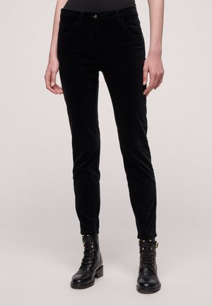 Pantalones de pana negros con un corte ajustado, que cuentan con bolsillos delanteros, cremallera y una textura suave. Combinados con botas de combate negras.