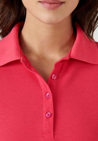 Polo shirt rosa con un tessuto testurizzato, dotato di colletto e tre bottoni rosa coordinati al colletto. La vista ravvicinata mette in risalto i dettagli.