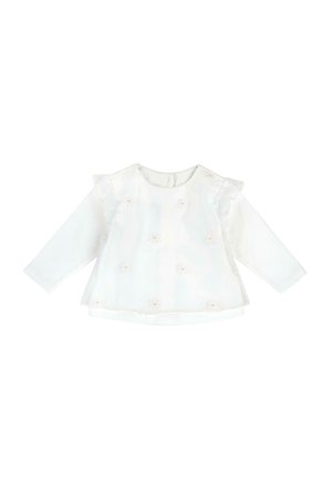 Biała, długorękawowa bluzeczka dla niemowląt z przezroczystą nakładką, małymi różowymi haftowanymi kwiatami i falbankami na ramionach na jednolitym tle.